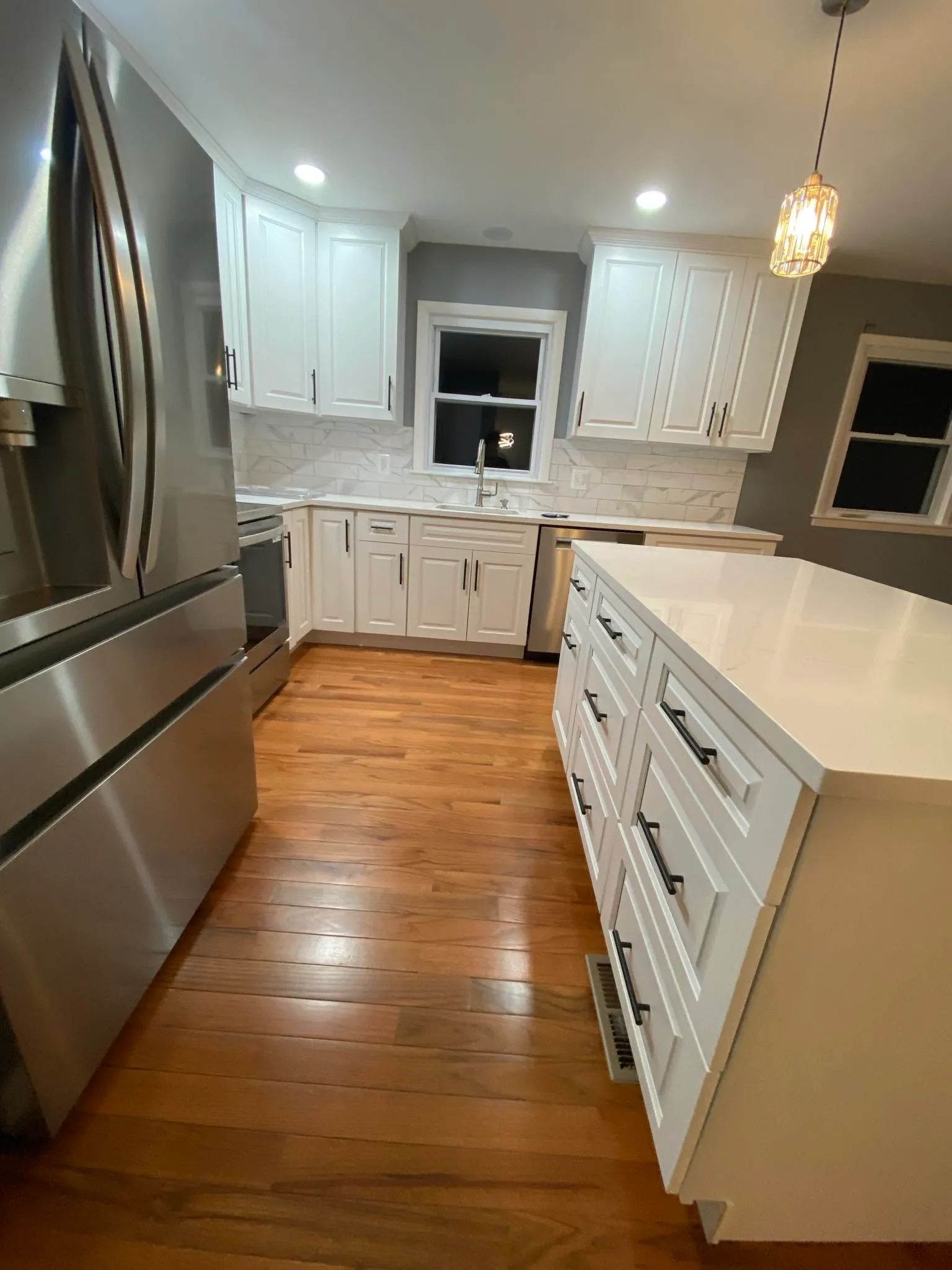 White kitchen with quartz island, pendant lights, and hardwood floor